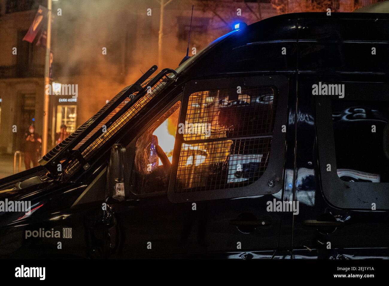 A riot police van is pictured on Passeig de Gràcia next to a burning barricade during the protest. Fifth night of protests and riots in response to the arrest and imprisonment of rapper Pablo Hasel accused of exalting terrorism and insulting the crown for the content of the lyrics of his songs. Stock Photo