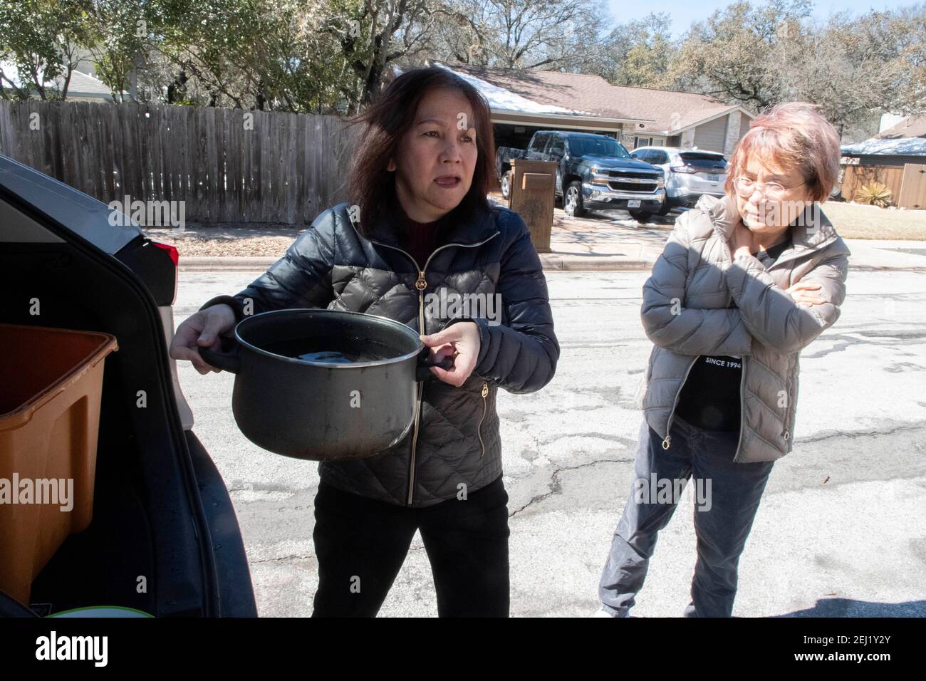 Austin, Texas USA Feb. 20, 2021: Homeowner Hank Lam carries a pot of water from the rear of a friend's SUV heading toward her house during a water emergency in central Texas. Unusually low temperatures caused frozen and broken water pipes throughout the area, leaving residents without running water and sending them scrambling for potable water. Credit: Bob Daemmrich/Alamy Live News Stock Photo