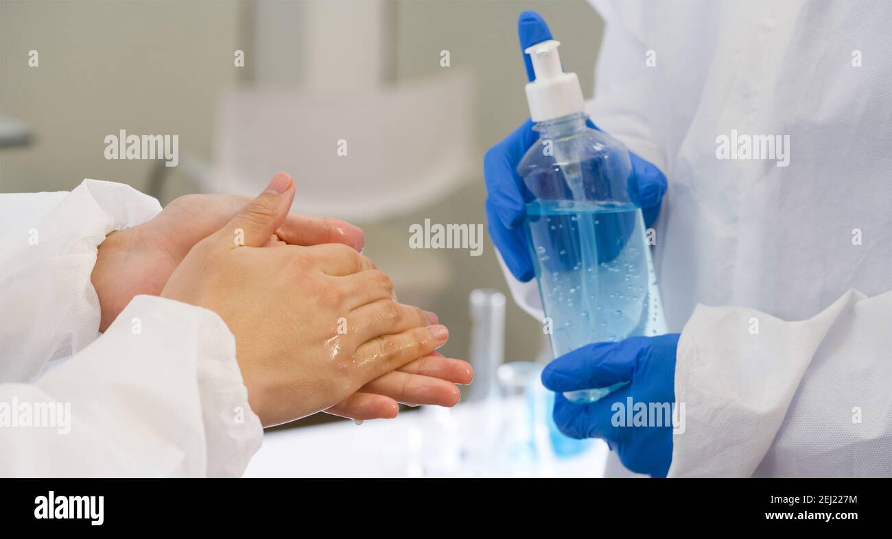 Epidemiological researchers in virus protective clothing washing hands with alcohol gel before beginning the experiment in a scientific laboratory. Hy Stock Photo