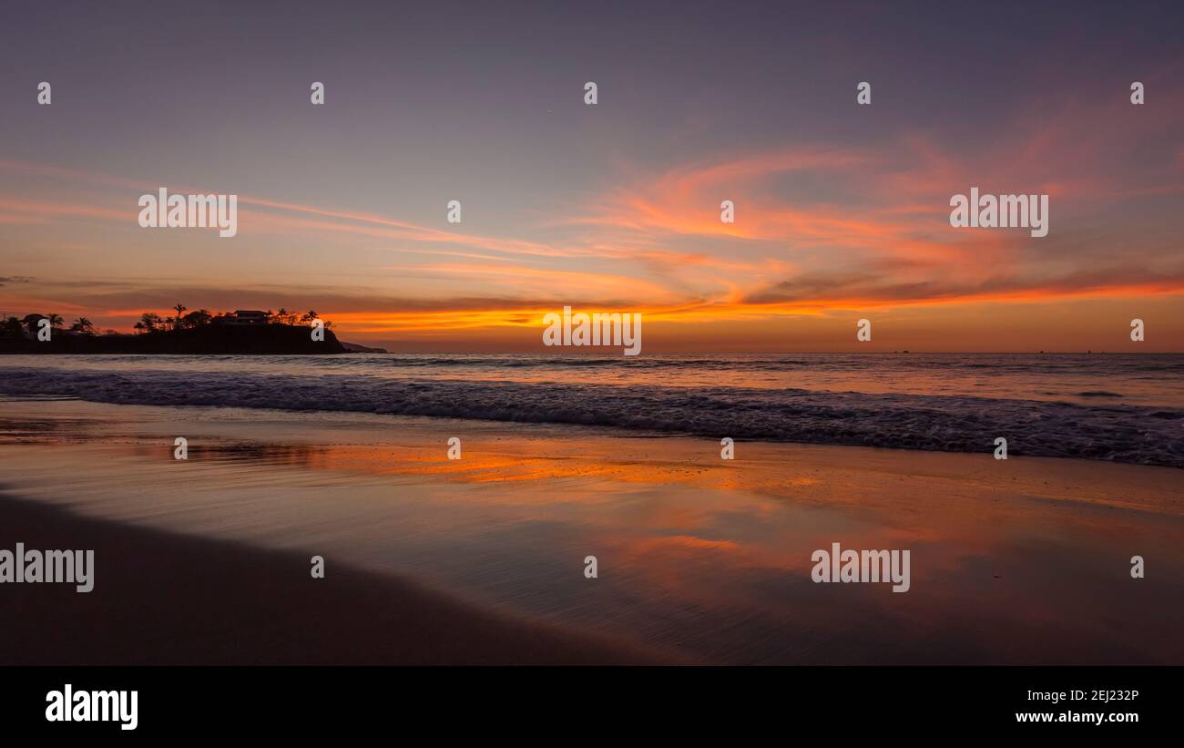 Tropical summer calm sunset landscape at the beach with sand, water, ocean waves, sky with orange curved clouds reflected on the sand, Costa Rica Stock Photo