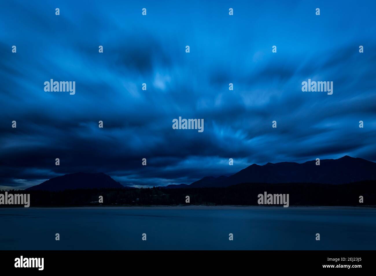 Long exposure blue hour landscape with a looming cloudy sky, Lake Koocanusa on the foreground and mountains on the background, BC, Canada Stock Photo