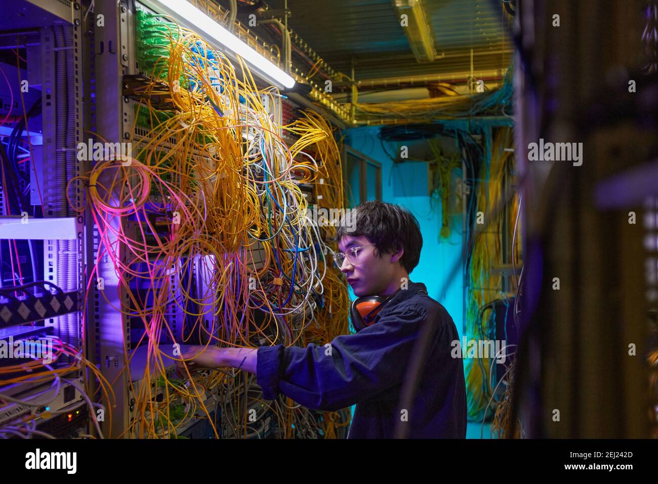 Side view portrait of young network technician connecting cables in server room, copy space Stock Photo
