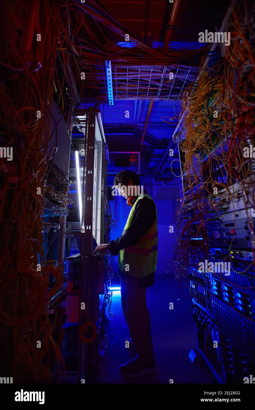 Futuristic side view at young network technician using laptop in server room while setting up internet connection Stock Photo
