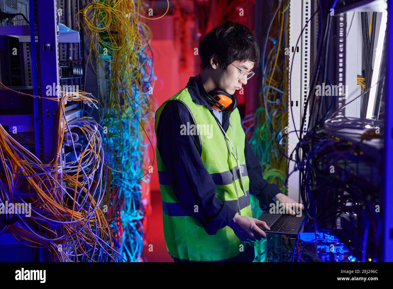 Side view portrait of young network technician using laptop in server room while setting up internet connection, copy space Stock Photo