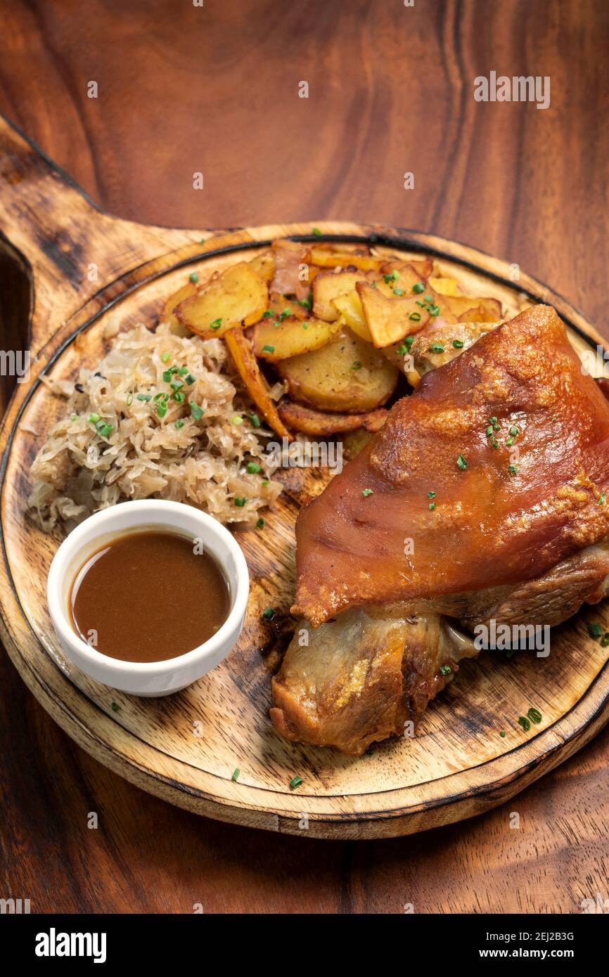 SCHWEINSHAXE traditional german pork knuckle with sauerkraut and potatoes bavarian meal on rustic wood background Stock Photo