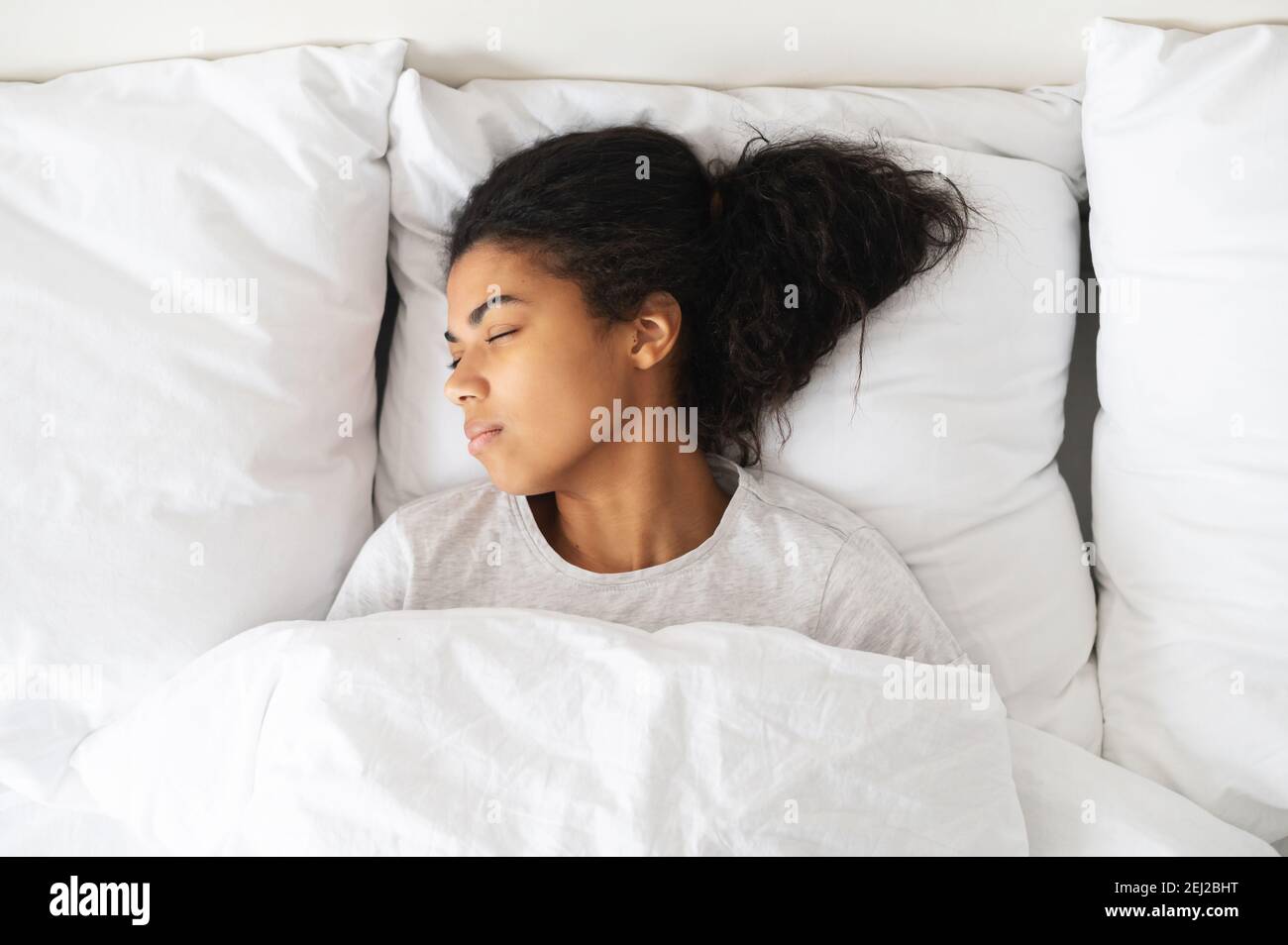 Healthy peaceful girl sleeping well in comfortable cozy fresh bed on soft pillow white linen orthopedic mattress, enjoy sleep at home, top view Stock Photo