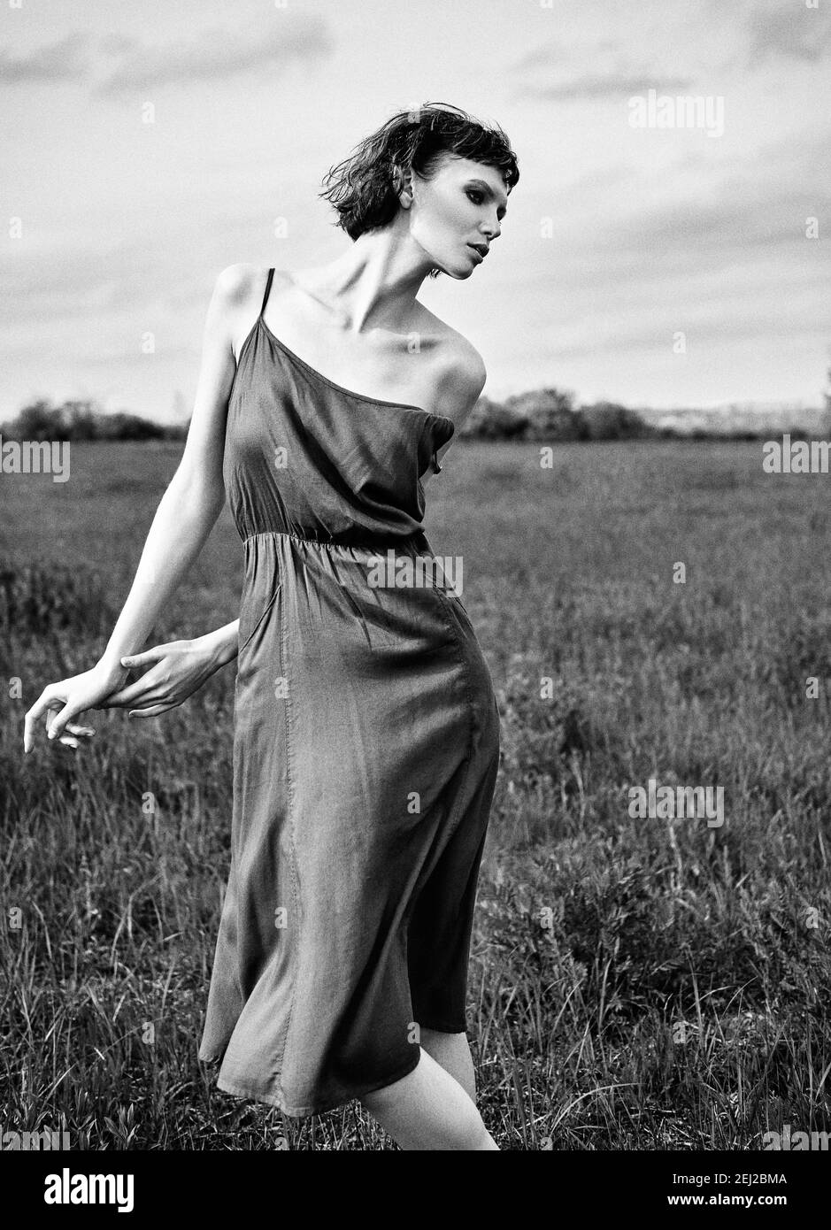 Outdoor fashion shot: beautiful sad girl in the field. Portrait of pretty young woman in dress. Black and white. Film grain effect Stock Photo