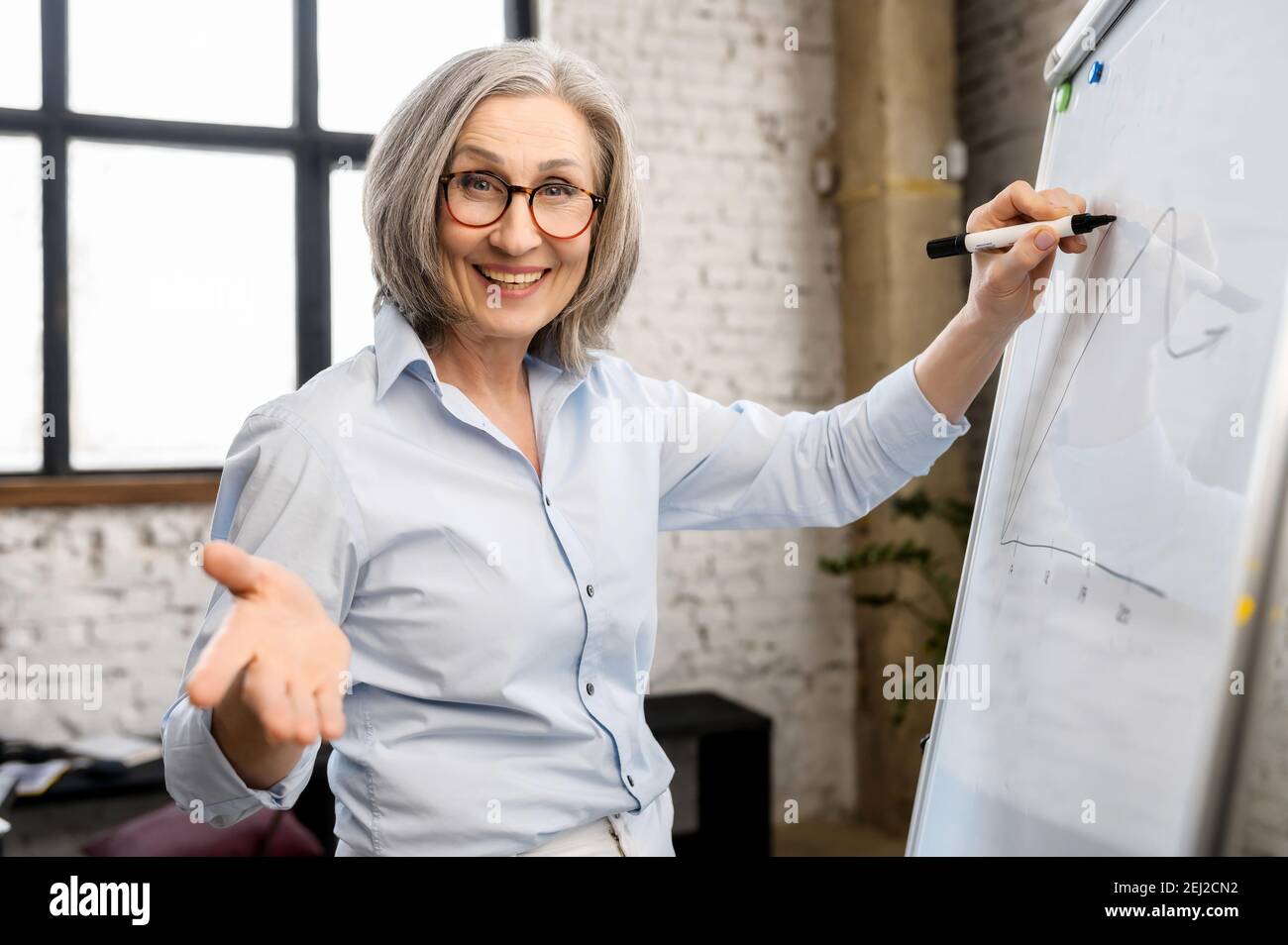 Modern mature gray-haired female school teacher, professor, college tutor  or coach looking at webcam and writing on the whiteboard, talking in Stock  Photo - Alamy