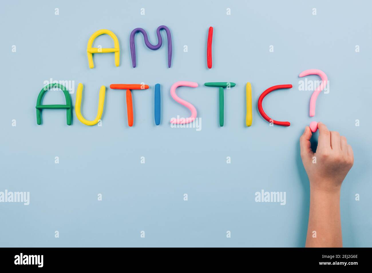 World Autism Awareness Day concept, symptoms - multicolored letters, Am I Autistic - on light blue background with child hand. Autism spectrum Stock Photo