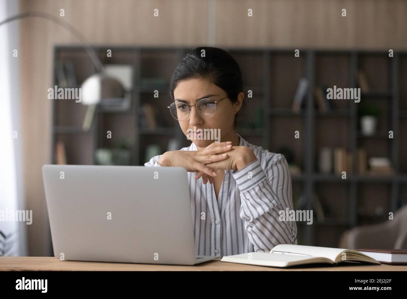 Pensive Indian woman look at laptop screen studying online Stock Photo ...