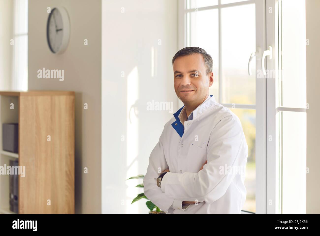 Smiling scientist or doctor in white coat standing arms crossed in laboratory or hospital Stock Photo