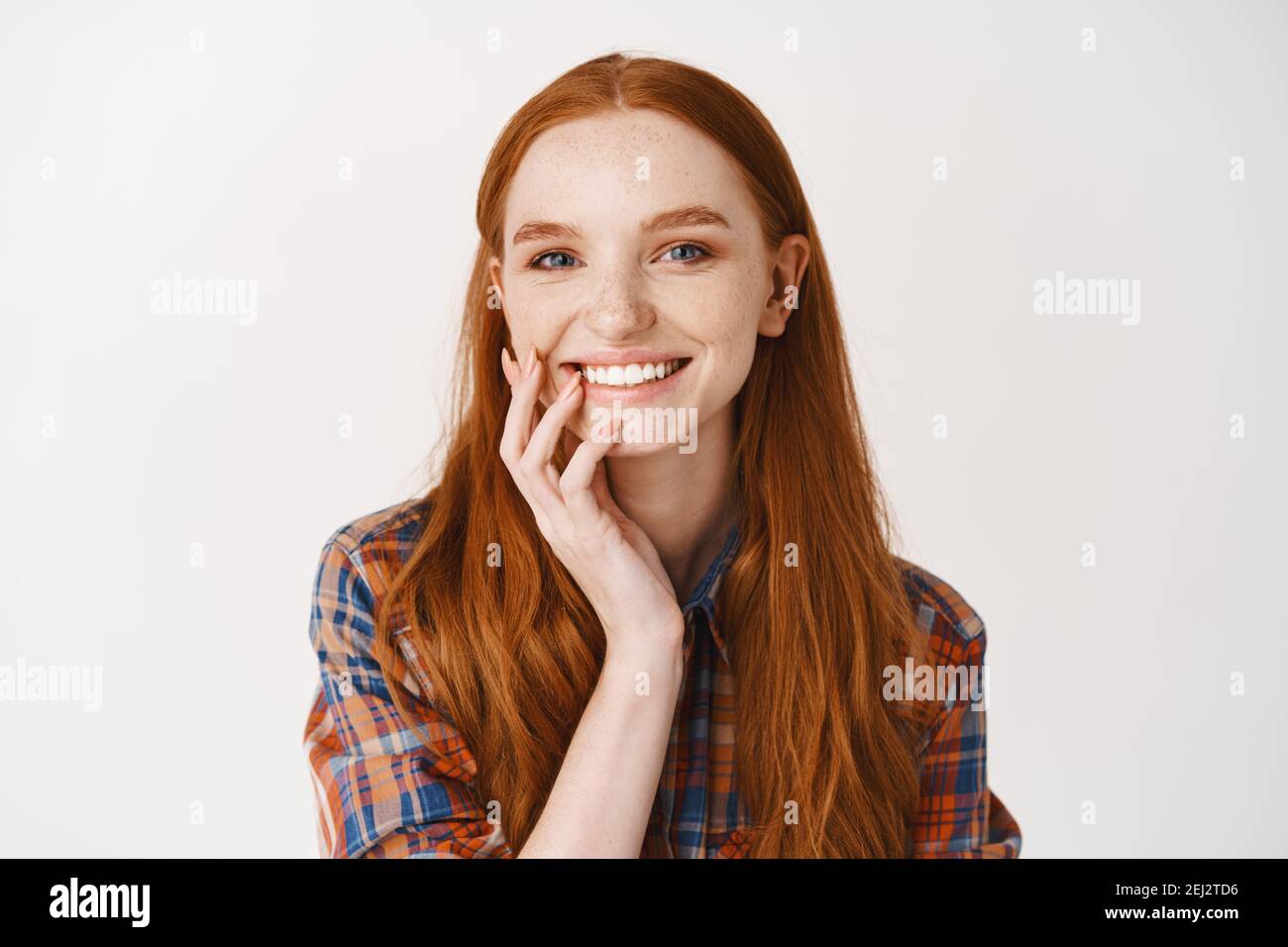 Close-up of redhead female without make-up and white perfect smile, looking happy at camera, standing against white background Stock Photo