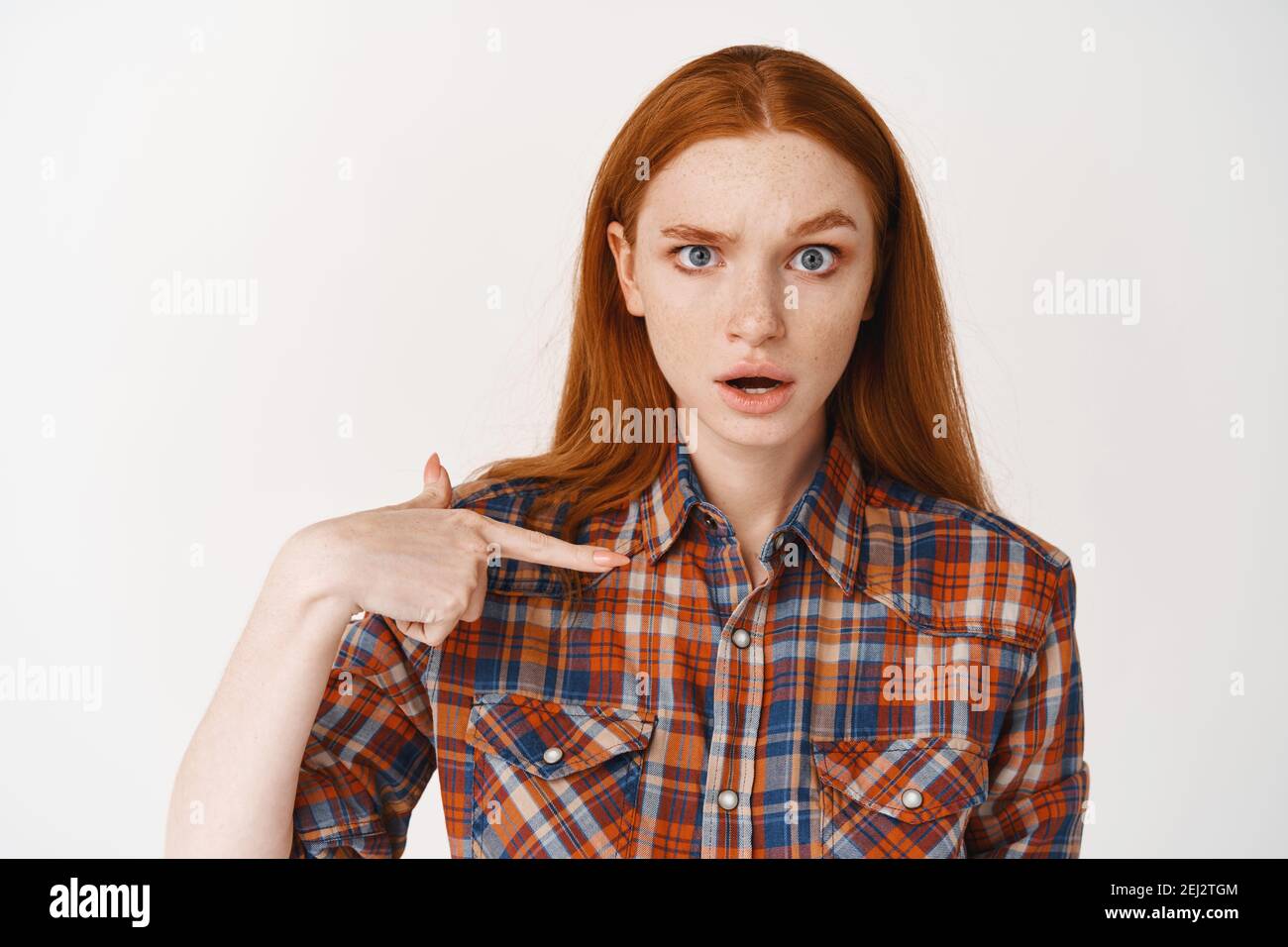 Close-up of redhead girl with pale skin looking confused, pointing at herself puzzled, standing on white background Stock Photo