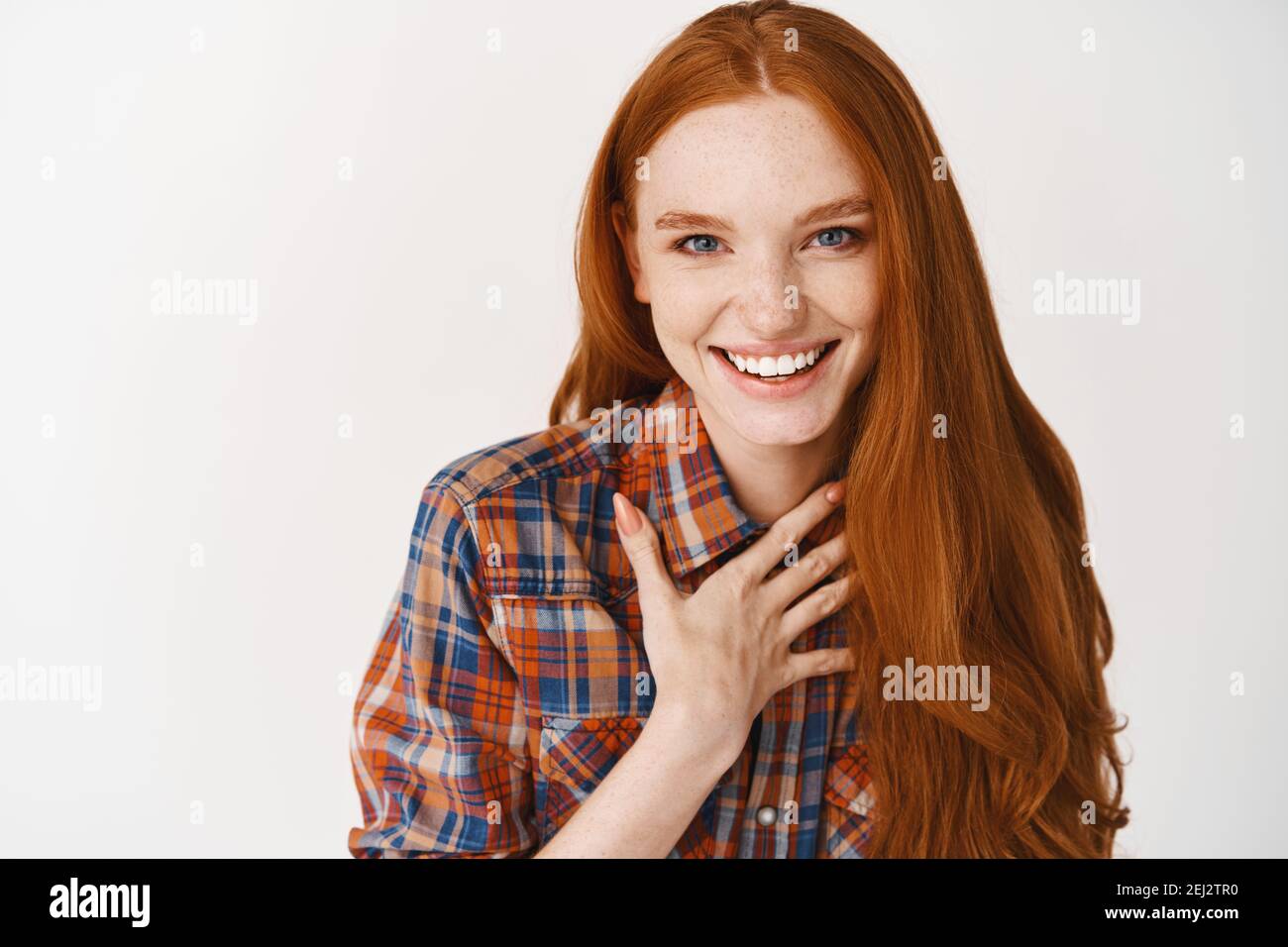 Close-up of beautiful redhead woman with pale skin and blue eyes, touching heart and smiling, thanking you, standing grateful against white background Stock Photo