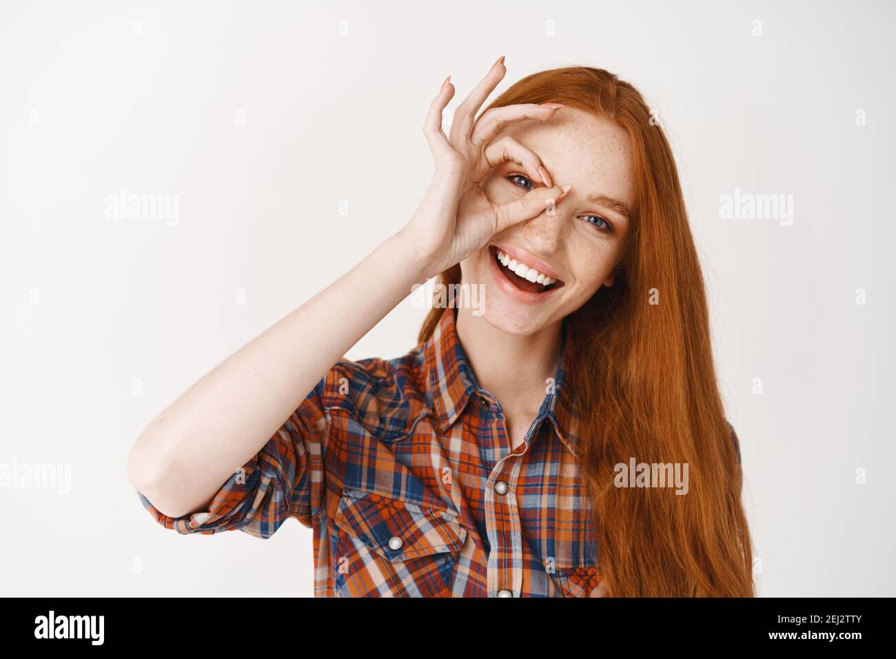 Close-up of beautiful redhead woman smiling with white teeth, showing okay sign and looking happy, standing over white background Stock Photo