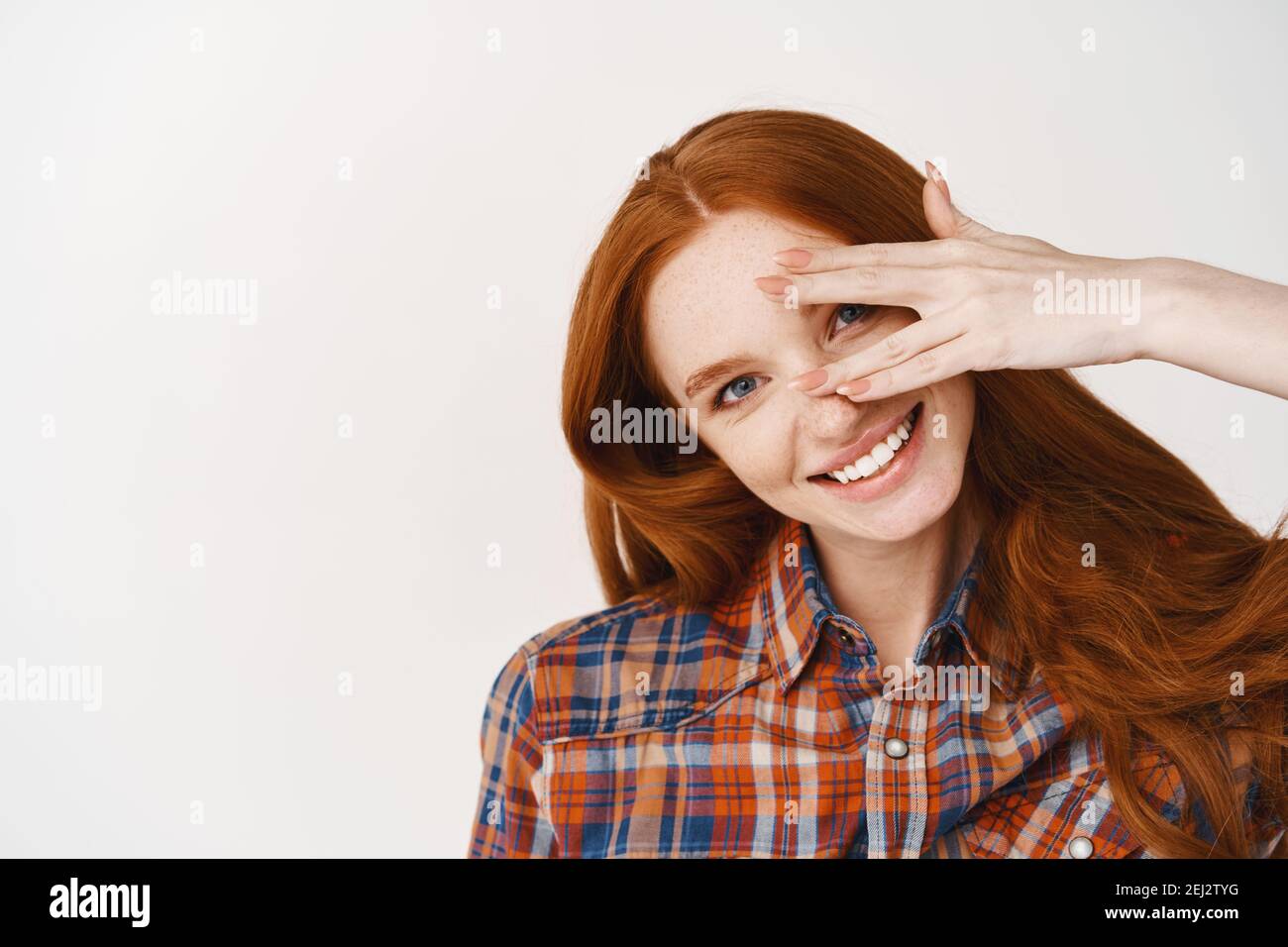 Close-up of beautiful redhead lady with blue eyes and pale skin, smiling at camera, standing over white background Stock Photo