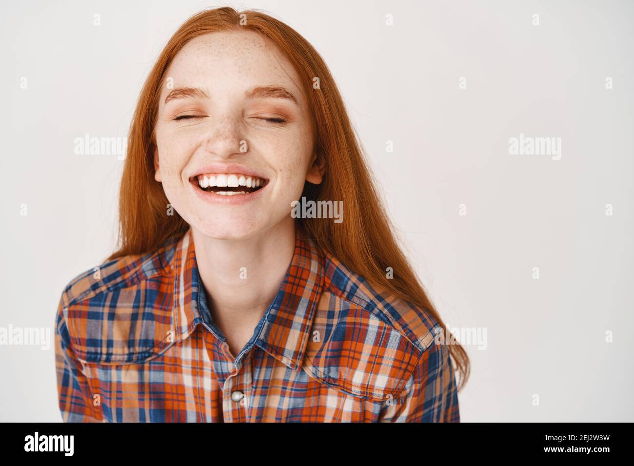 Close-up of beautiful redhead woman laughing with closed eyes, standing over white background Stock Photo