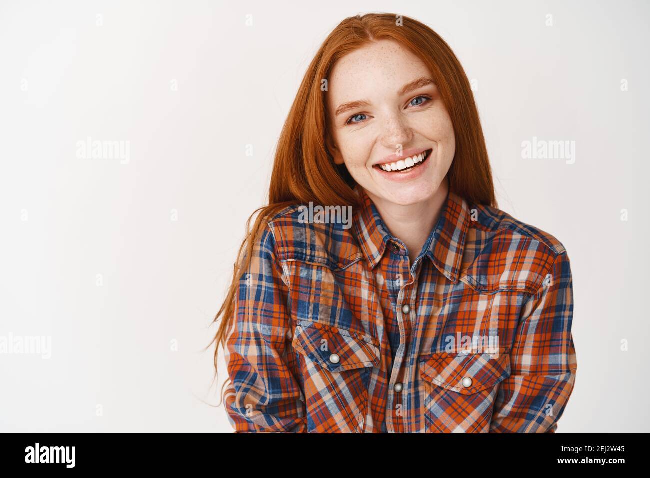 Young redhead woman with pale skin and white smile looking happy at camera, standing over white background Stock Photo
