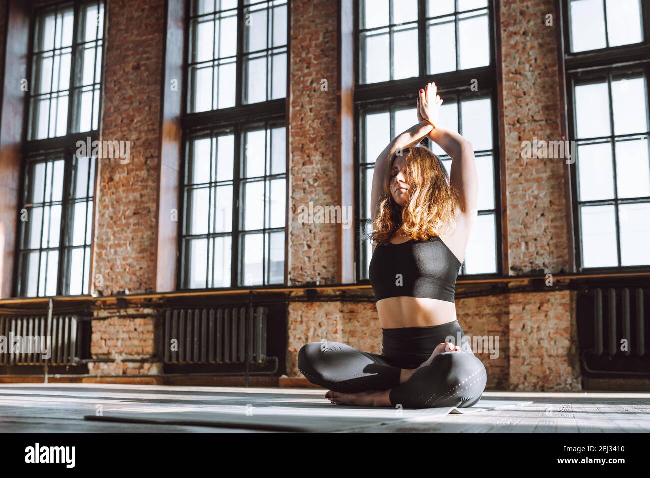 Young curly female sit in lotus pose on floor of loft studio with big ...
