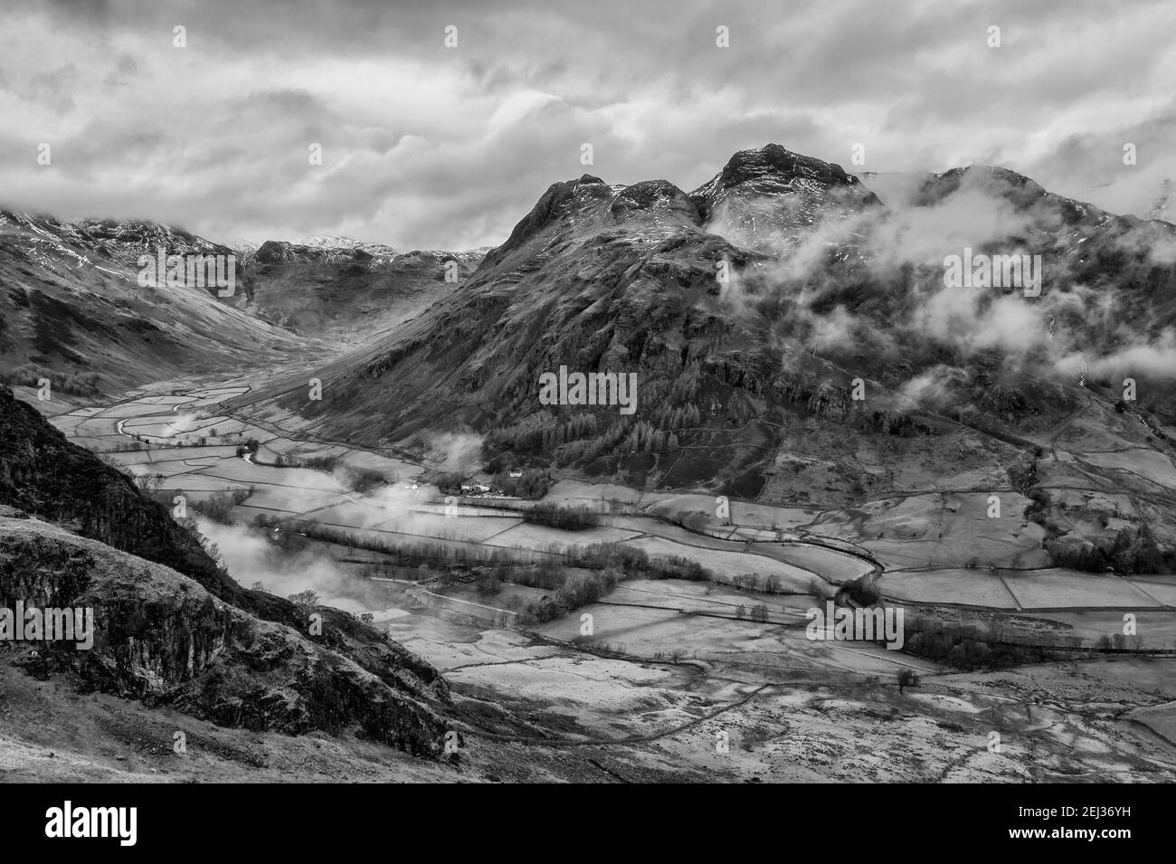 Epic flying drone  black and white landscape image of Langdale pikes and valley in Winter with low level clouds and mist swirling around Stock Photo