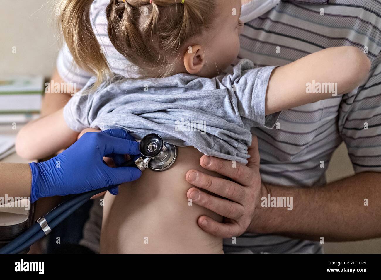 Little girl in the arms of her father in the doctor's office at the clinic. The doctor examines the child, listens to the lungs with a phonendoscope. Stock Photo