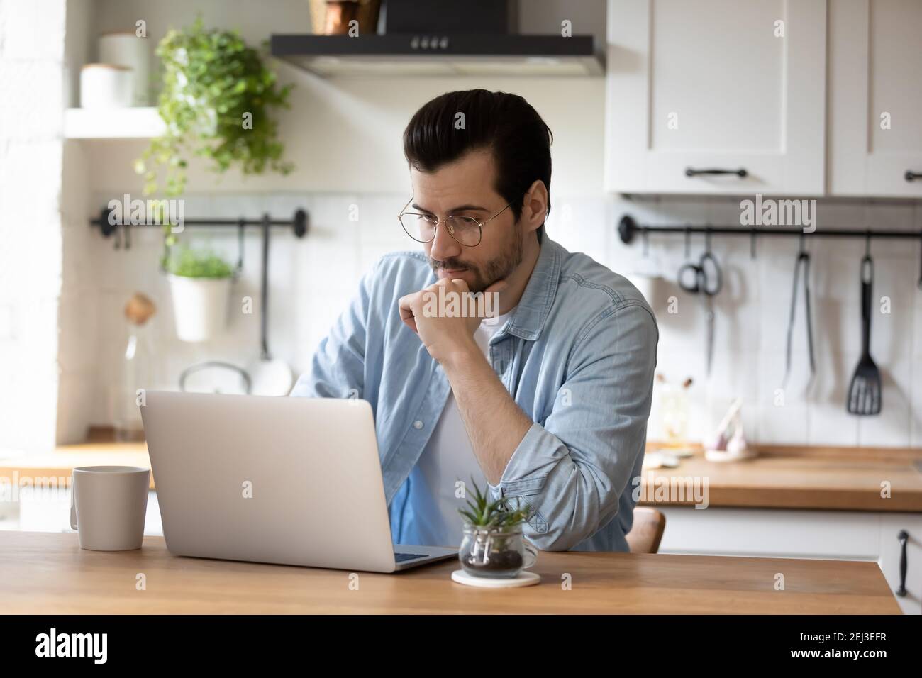 Pensive young man work on laptop at home kitchen Stock Photo
