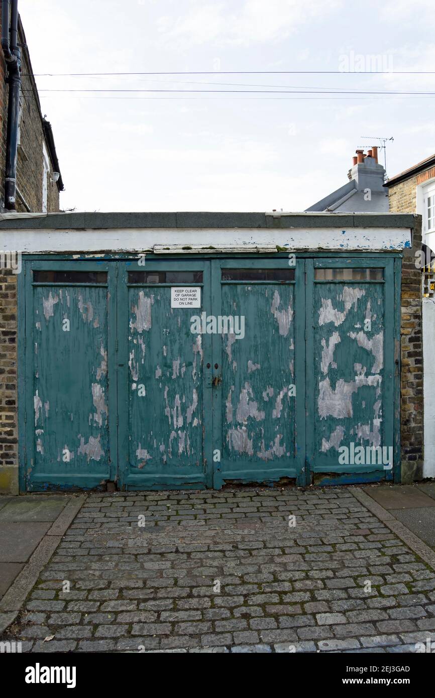 residential garage frontage in putney, london, england, with peeling paint on rotting wooden doors and no parking notice Stock Photo