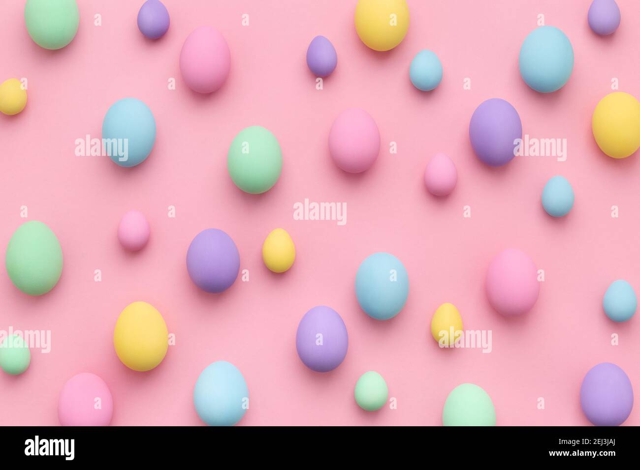 Pastel colored Easter eggs scattered on pink background. Easter Day colorful abstract flat lay. Stock Photo