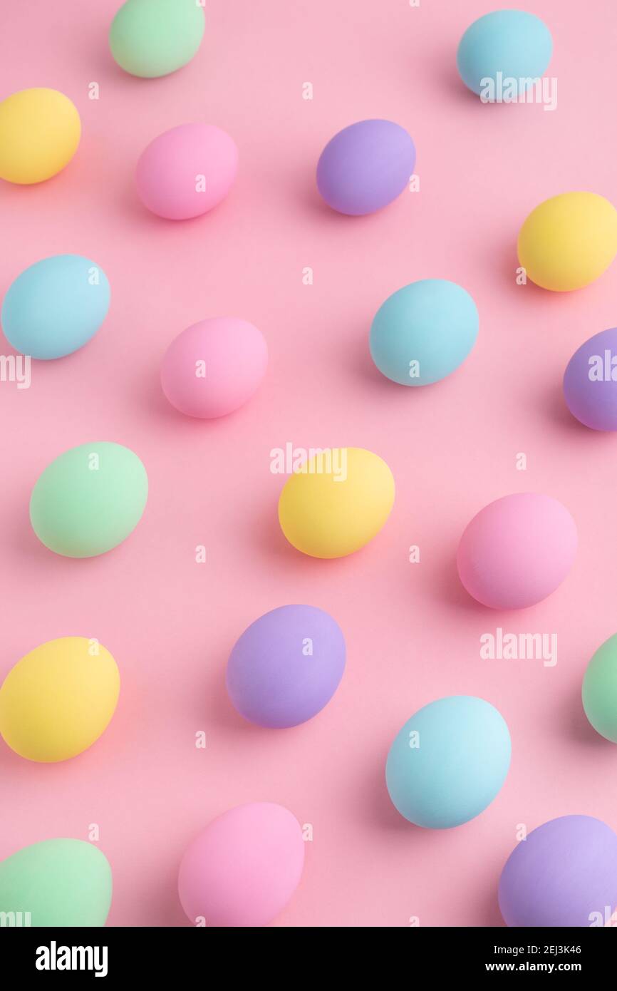 Pastel colored Easter eggs scattered on pink background. Easter Day colorful pattern, abstract flat lay. Stock Photo