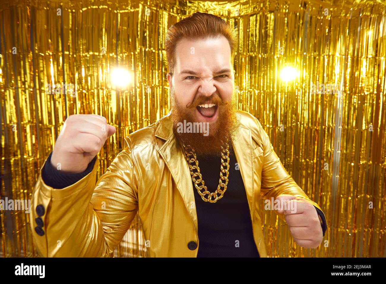 Funny bearded man in shiny golden jacket and gold chain having fun at disco party Stock Photo