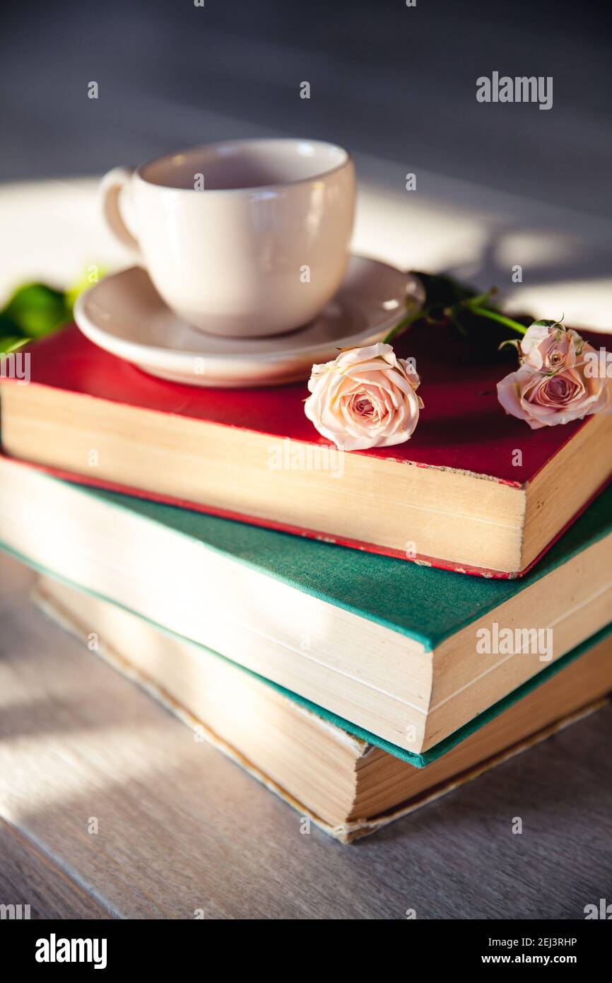 Beautiful bouquet of roses in the sun on the books with a cup and ...