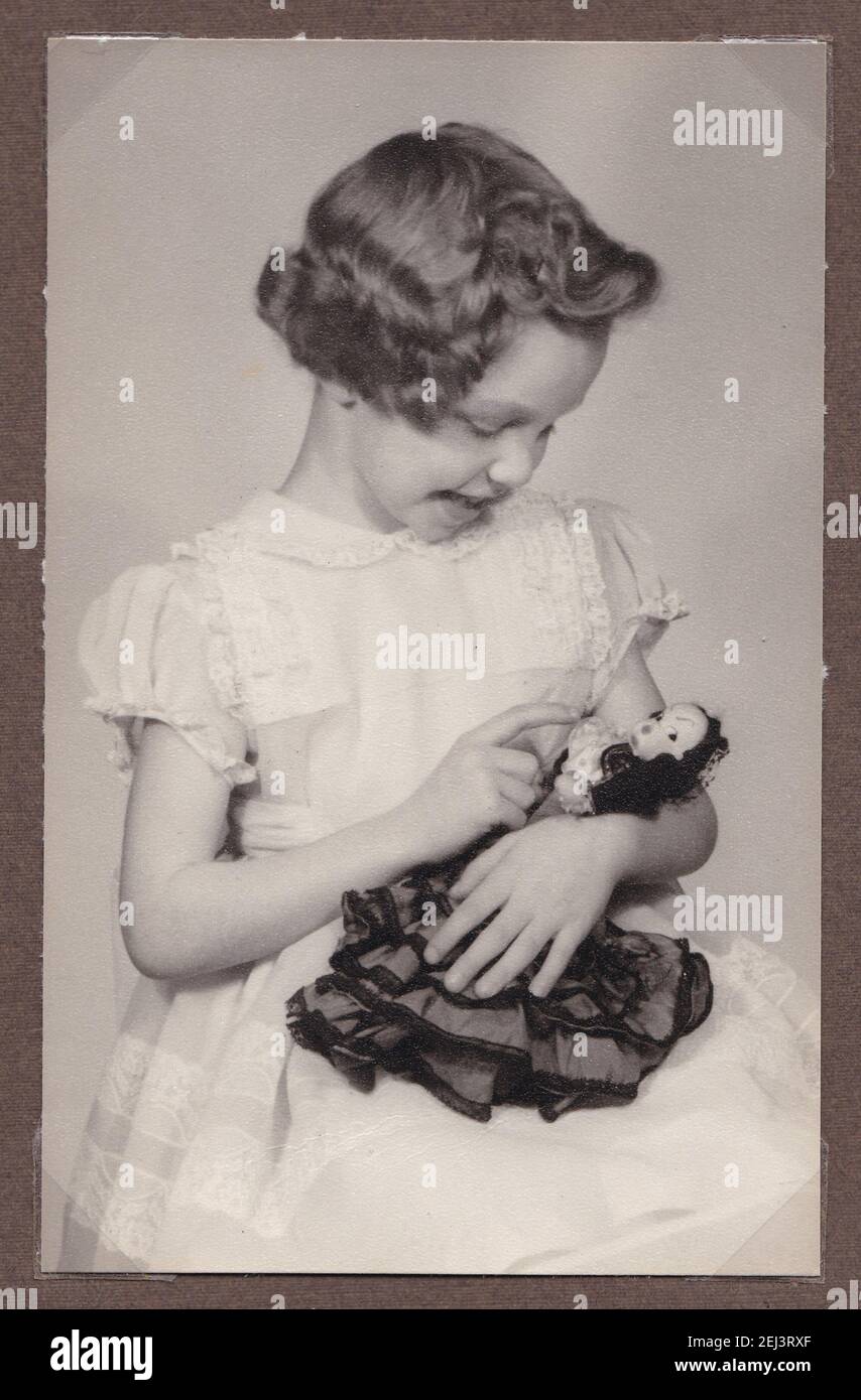 Vintage black and white photo of a beautiful little girl cuddling her doll 1930s. Stock Photo