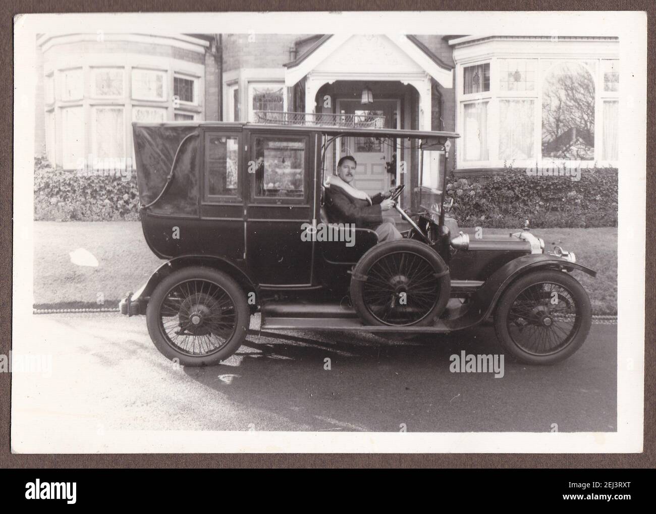 Vintage black and white photo of a man in a old antique car in front of house 1930s. Stock Photo