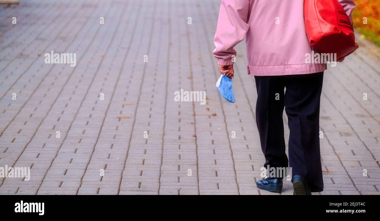 Woman walking on the street with protective face mask holding in hand Stock Photo