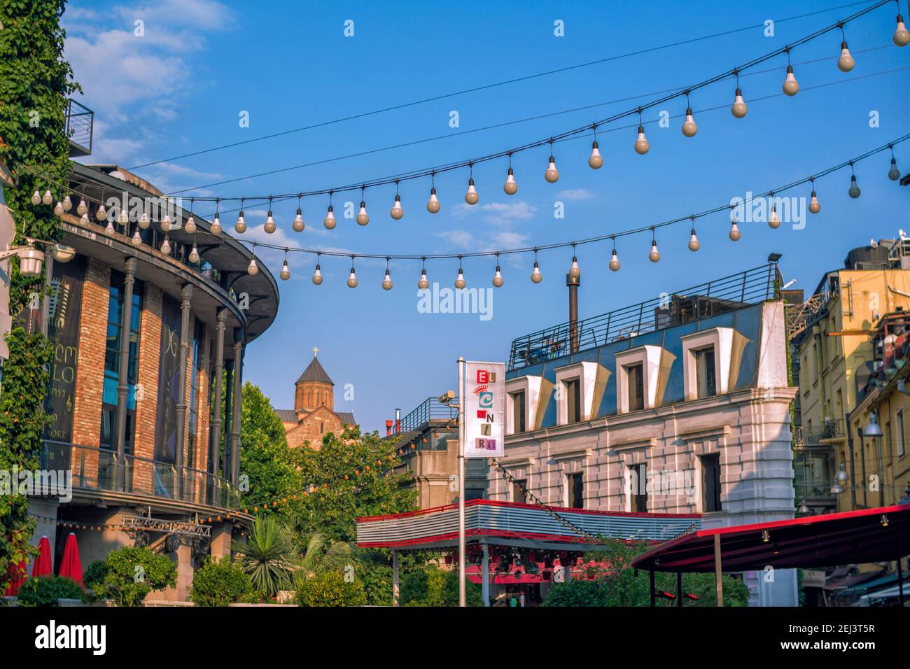 Tbilisi/Georgia – July 19, 2019: summer cityscape with modern architecture and Sioni Cathedral of the Dormition on the horizon. Lamps garland decorati Stock Photo