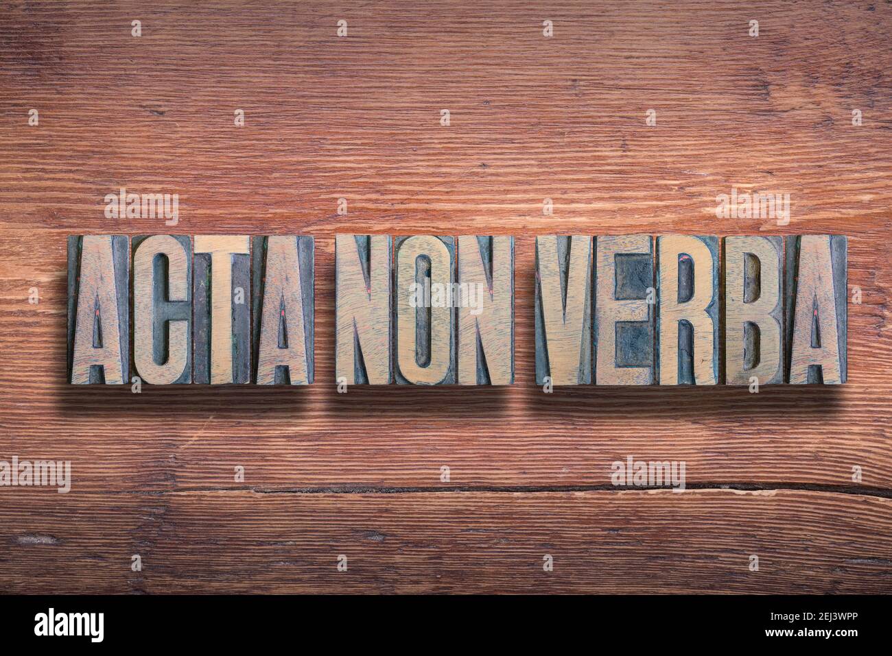 acta non verba ancient Latin saying meaning «deeds, not words» combined on vintage varnished wooden surface Stock Photo