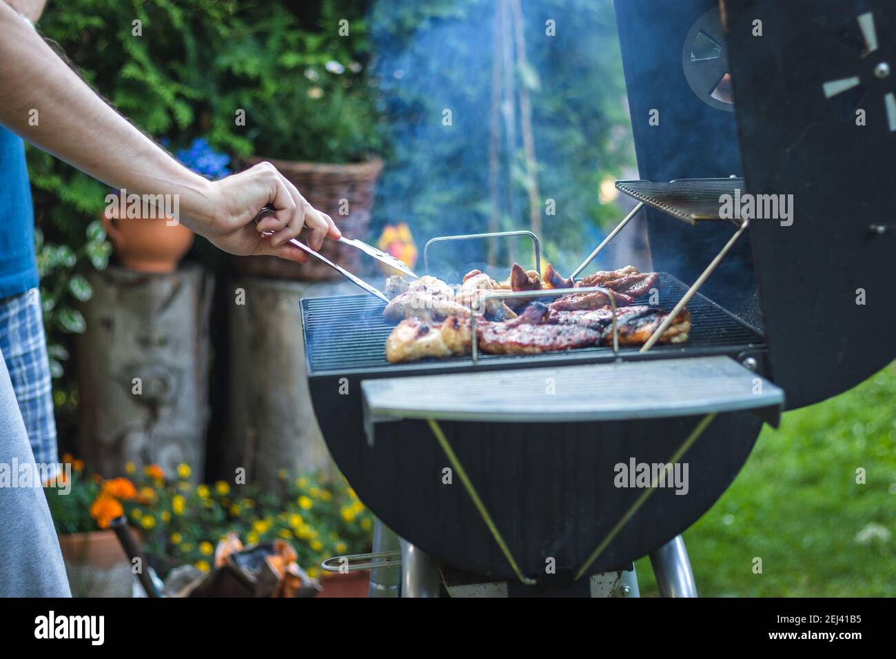 Barbecue meat on grill during garden party. Man cooking marinated food at summer bbq outdoors Stock Photo