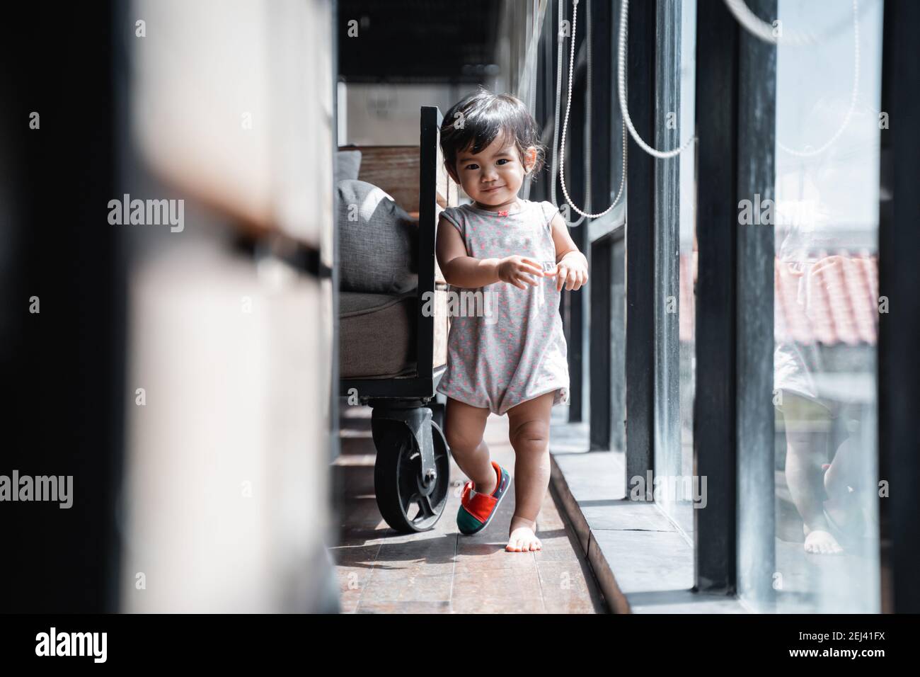 cute little baby walking in one shoe beside the glass window Stock