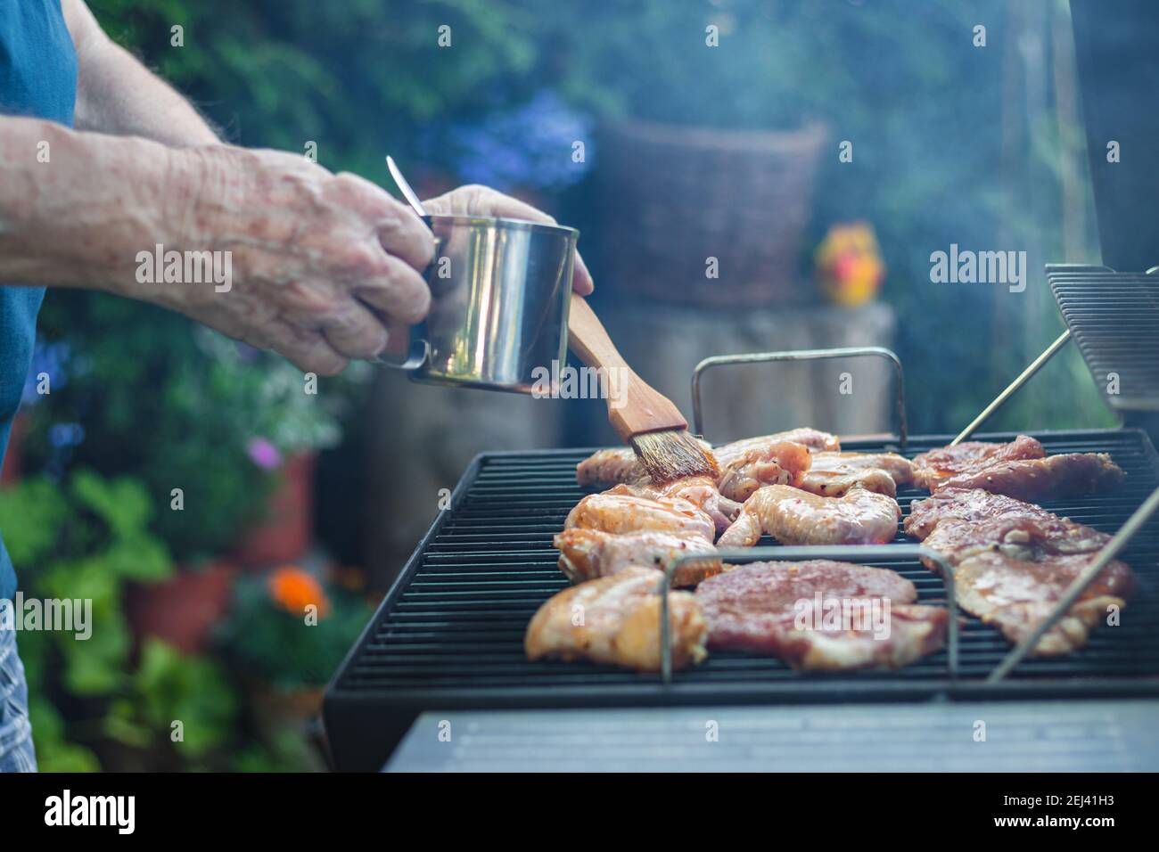 Marinated meat on grill during garden party. Summer barbecue outdoors. Man with basting brush marinate grilled food Stock Photo