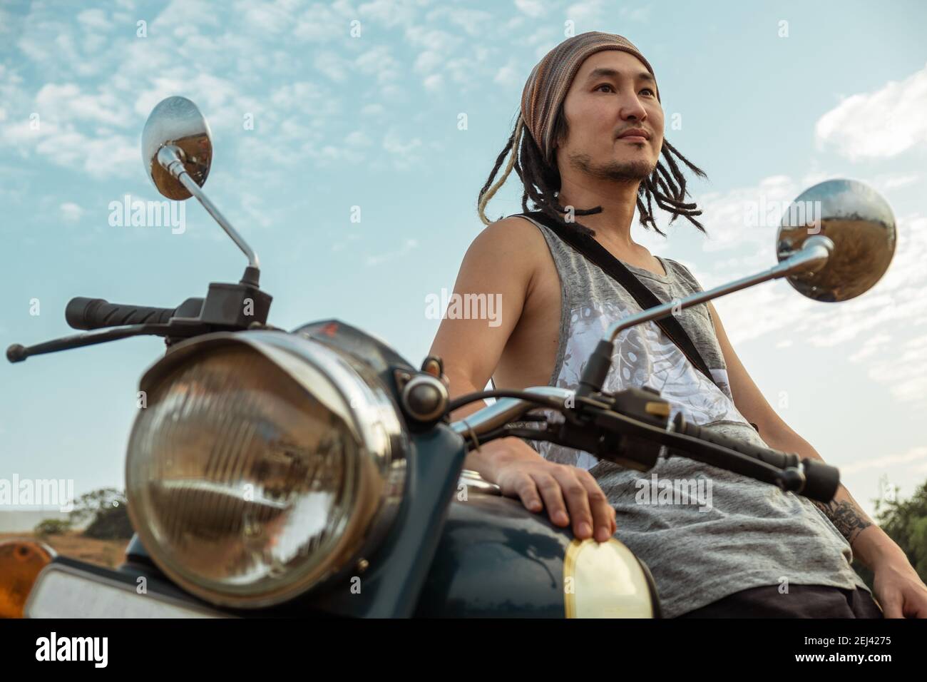 A man stands near a motorcycle in a field waiting for sunset, closeup, low point of view Stock Photo