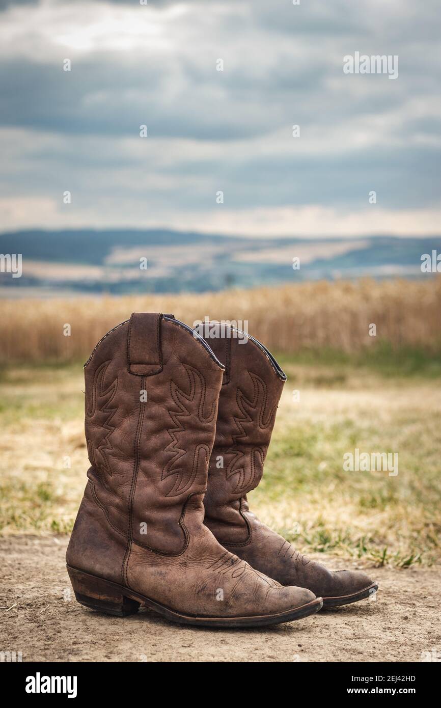 Cowboy boot in rural scene with moody sky. Old brown leather boots