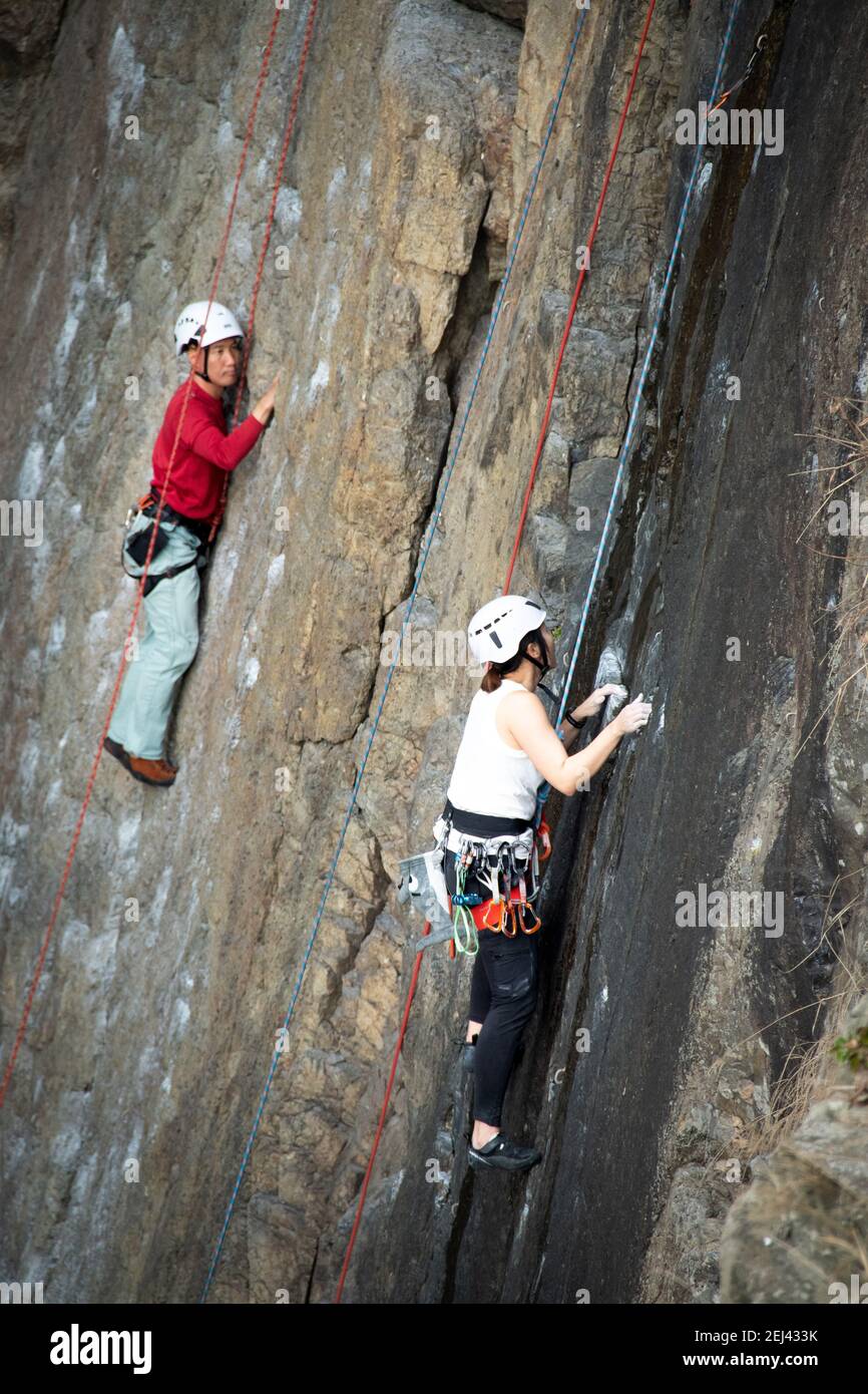 Asian girl and man climbing a vertical rock wall in Cape Collinson