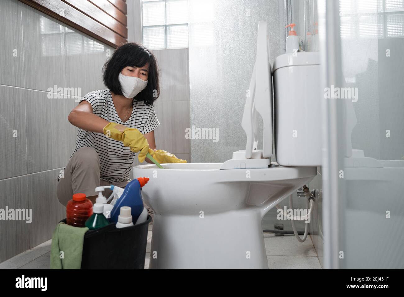 woman wearing mask wearing gloves brushing dirty toilet in bathroom