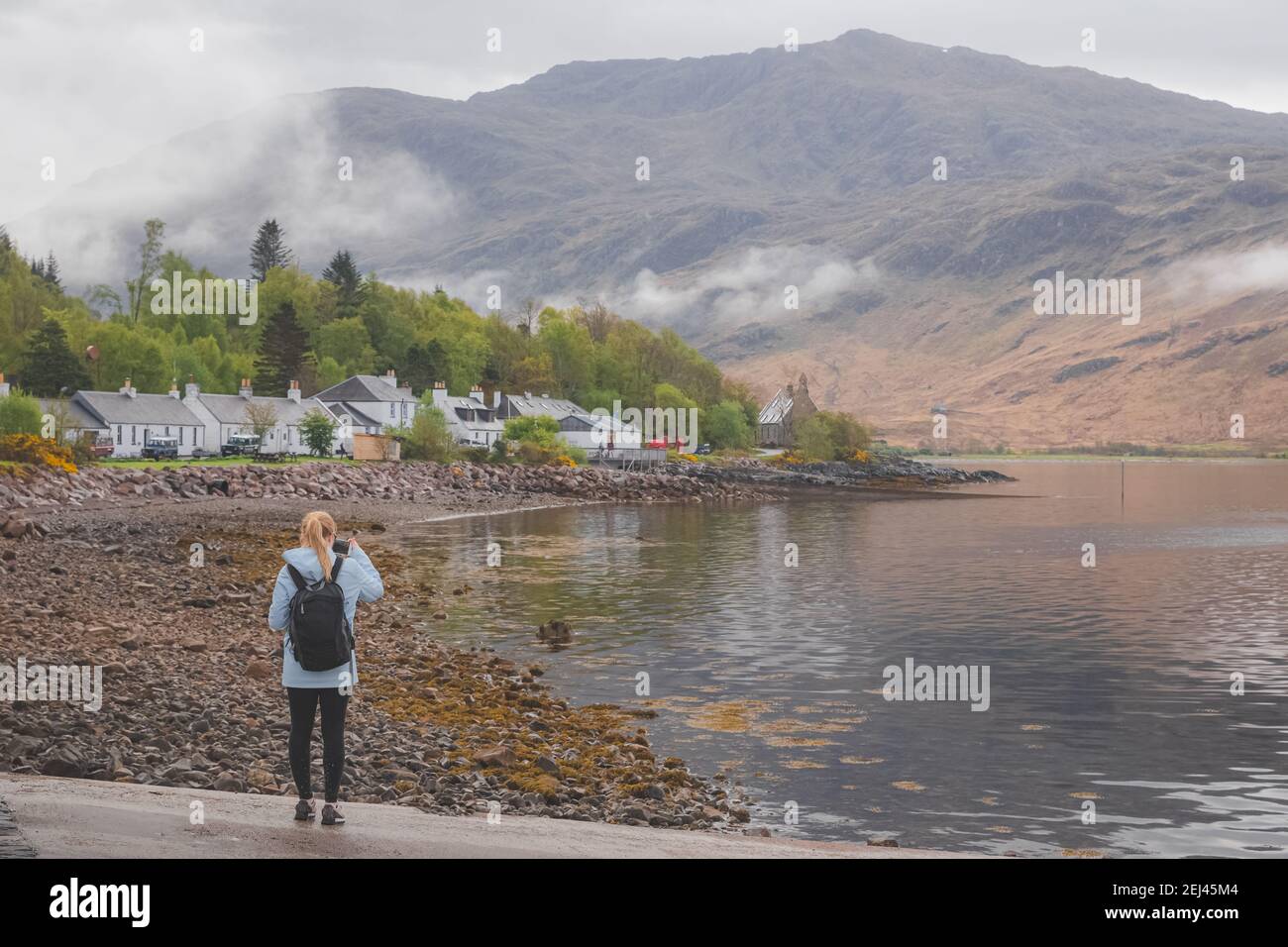 A young female tourist takes a photograph  of Inverie village on the remote Knoydart peninsula in the Scottish Highlands, west coast of Scotland. Stock Photo