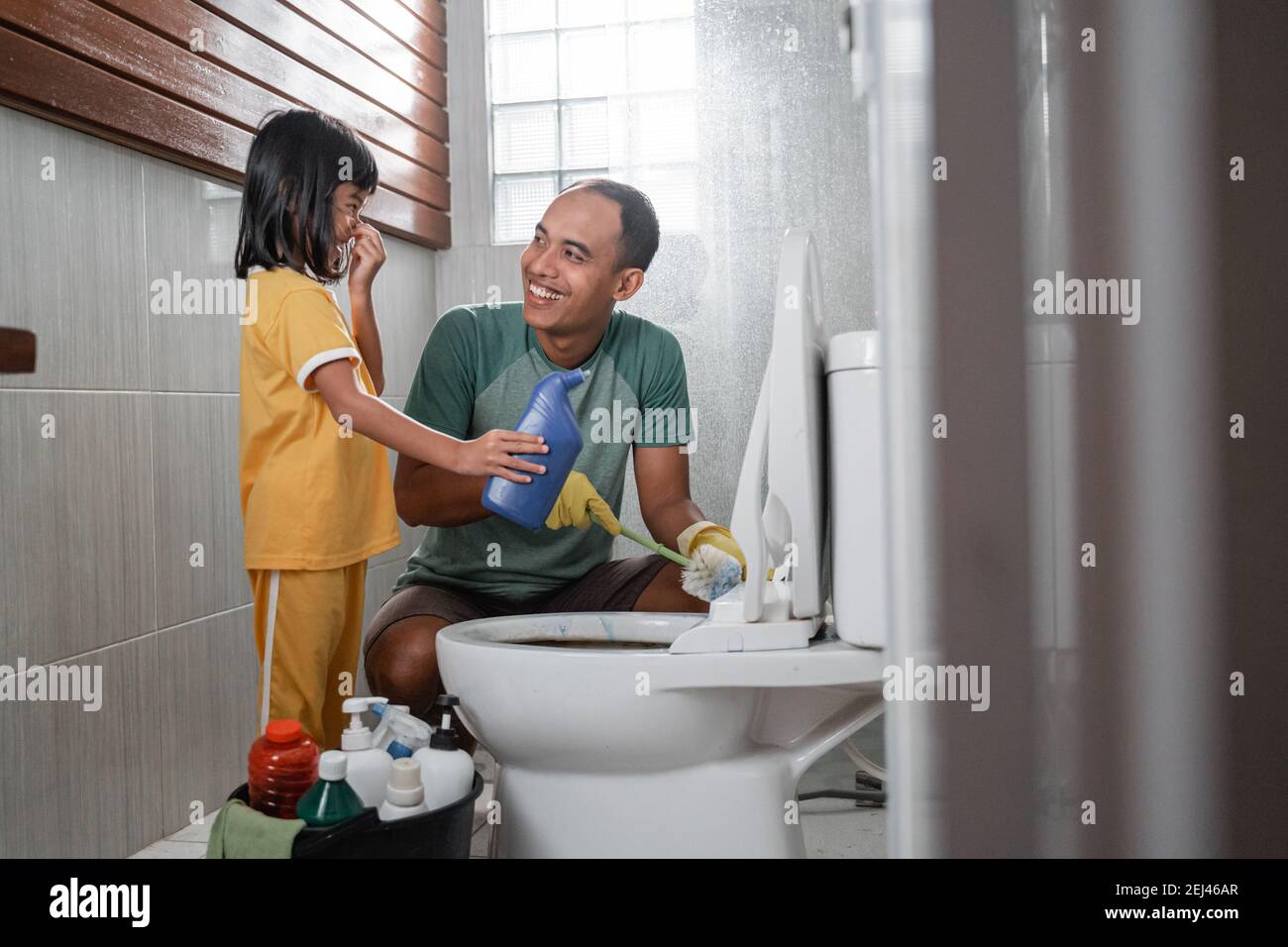 little girl holding bottle of cleaning liquid chatting with dad while  brushing dirty toilet in bathroom Stock Photo - Alamy