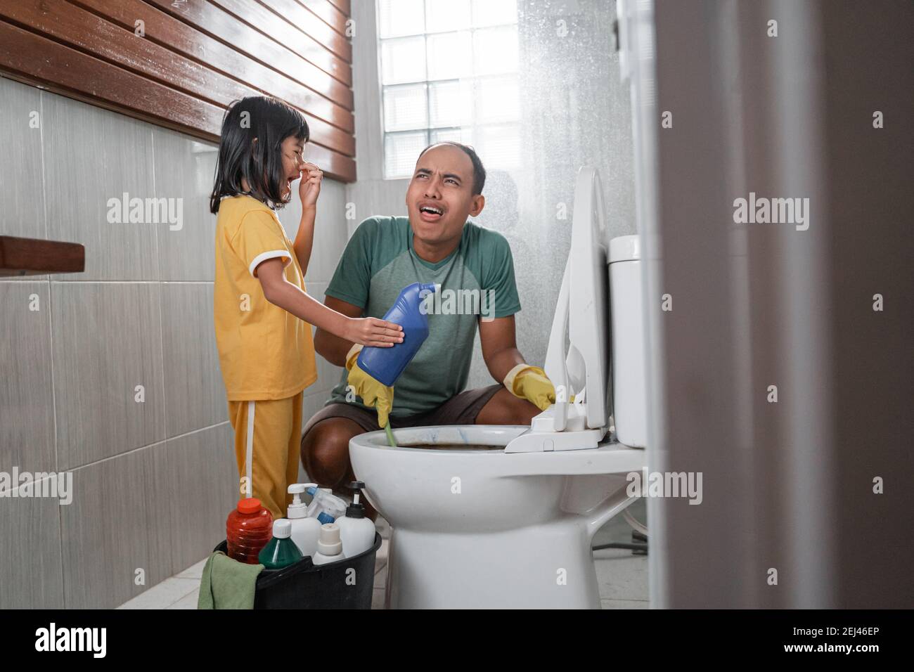 the little girl in a nasty pose holding a bottle of cleaning fluid chatting  with her dad while brushing the dirty toilet in the bathroom Stock Photo -  Alamy