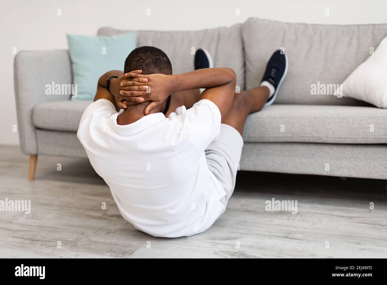 African Man Doing Abs With Legs On Couch At Home Stock Photo