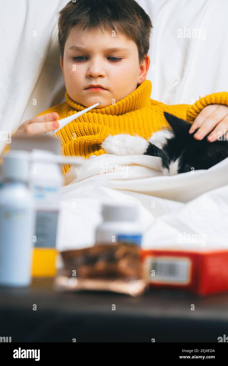 Sick child boy with digital thermometer in mouth lying in bed with fever illness headache stay