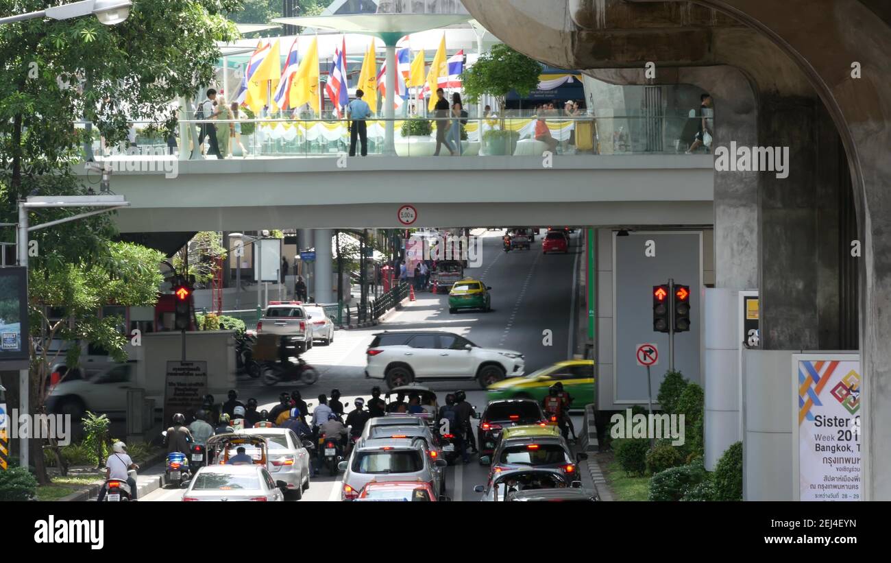 BANGKOK, THAILAND - 11 JULY, 2019: Intersection on busy city street. People on motorcycles and cars riding on crossroad under pedestrian bridge on bus Stock Photo