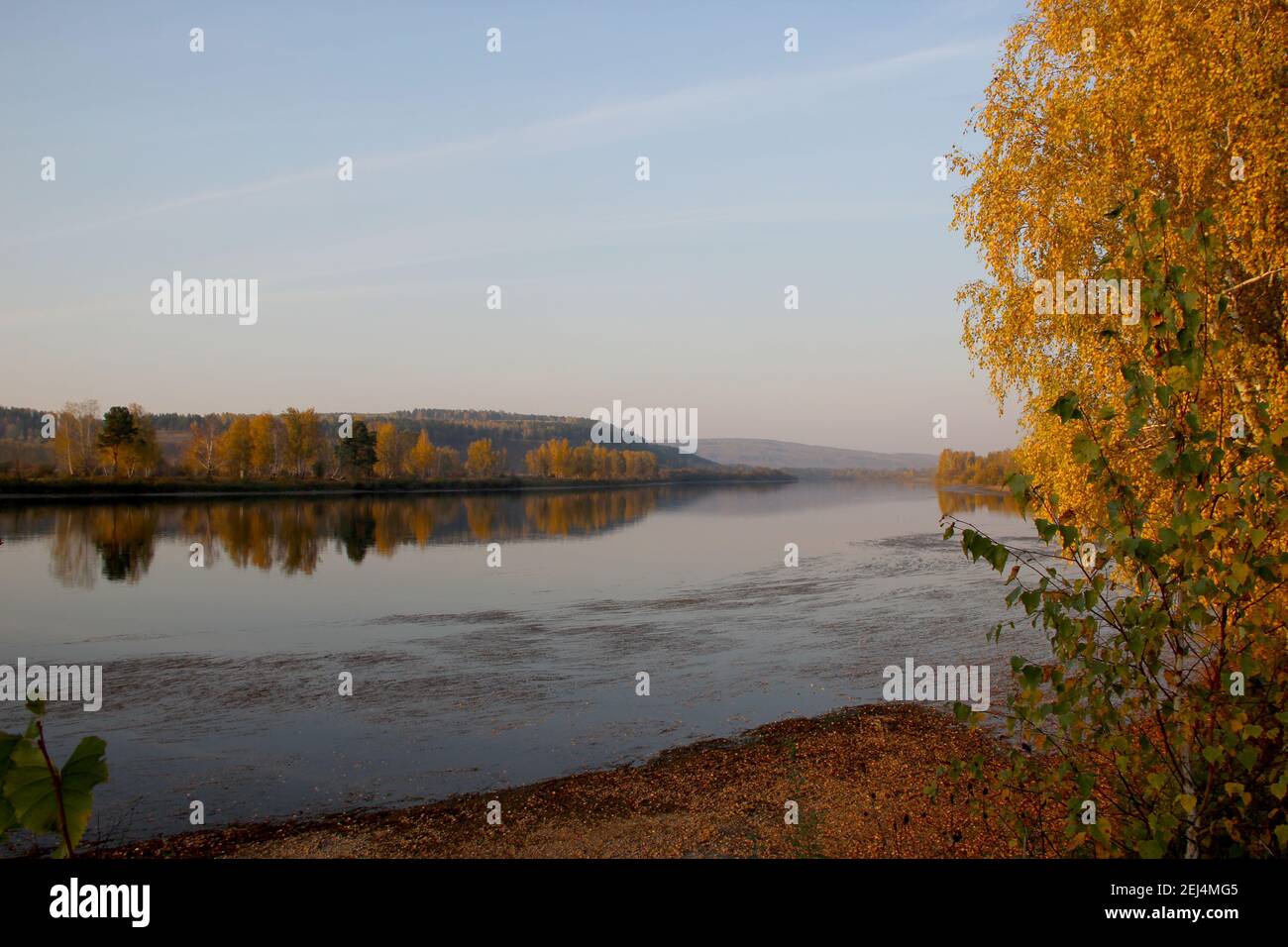 Beautiful autumn view from the shore on the river and hilly terrain. Reflection of colorful trees in the water. Stock Photo